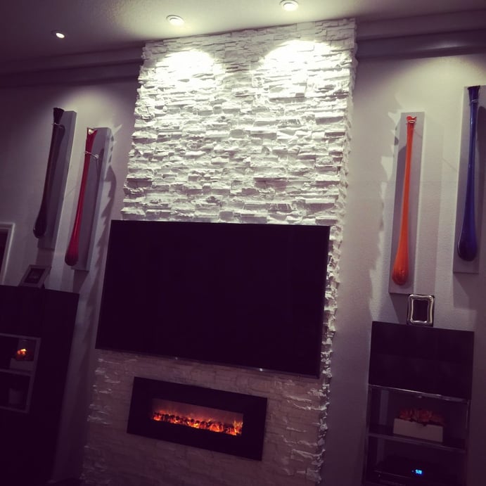 Lounge fireplace and TV surrounded with stone texture panels accentuated with overhead recessed lighting.