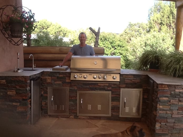 Outdoor BBQ island built from a wooden frame and finished with stacked stone panels to match a Southwestern style home.