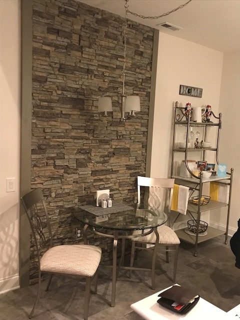 Accent wall made from stacked stone panels adds custom style to the kitchen of a cookie cutter house.