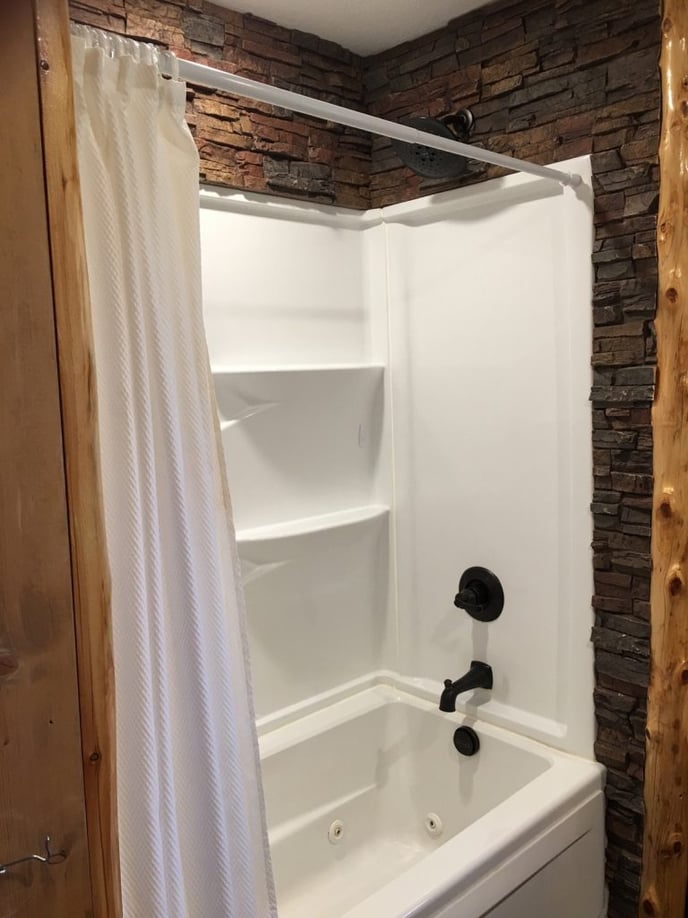White shower/bath cabinet adds a nice contrast to the surrounding stone-style wall.