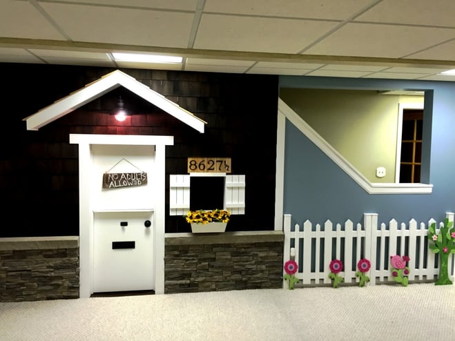 Basement playhouse complete with exterior wainscoting and white picket fence.