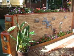 Outdoor divider wall doubling as a box planter covered in light tan stone wall siding.