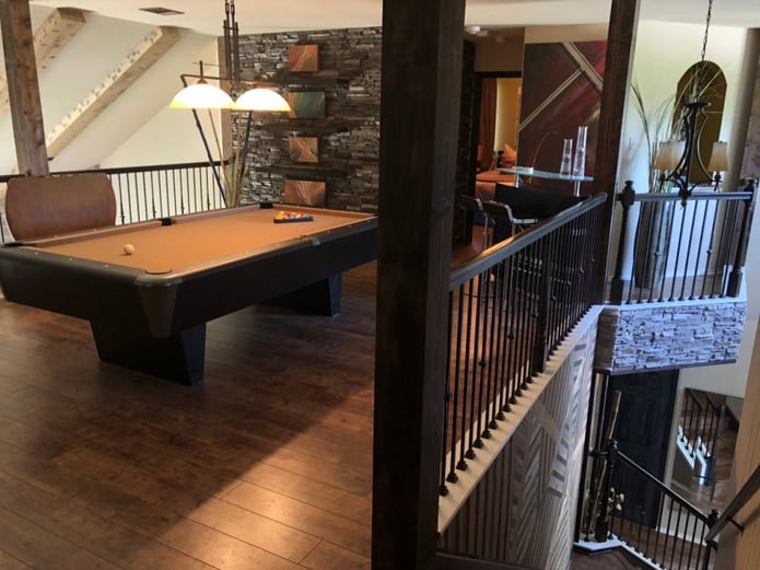 Home game room with hardwood floors, wrought iron railings and stacked stone panels on the wall.