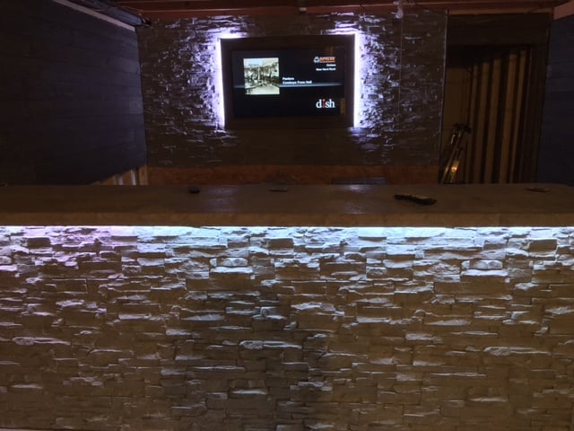 Home basement bar built with stacked stone panels, illuminated with hidden LED lights