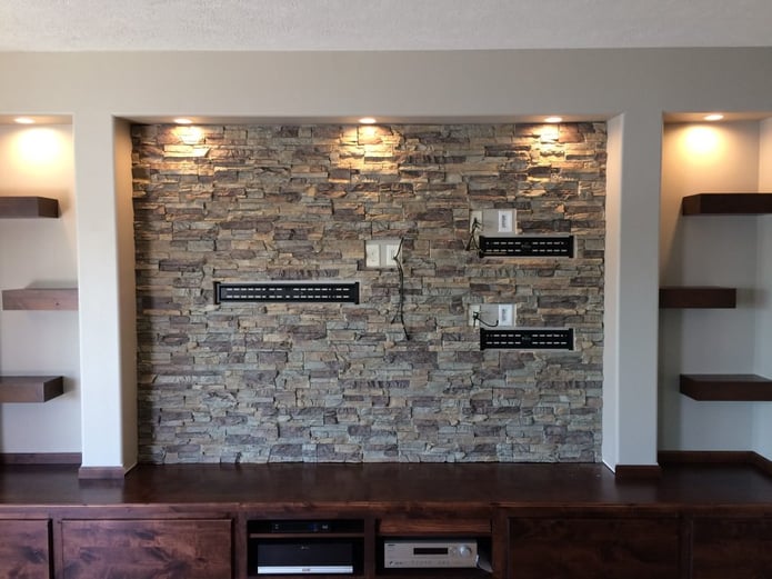Media center finished with stone style wall panels with holes cut out to accommodate mounting brackets.
