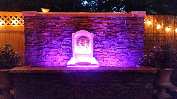 Outdoor water wall with stacked stone style finish is lit up at night with color-changing LED lights.
